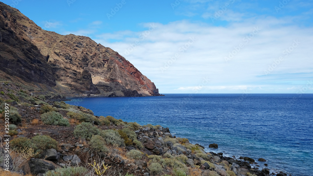 Solitary landscape of the wild south coast of the island of El Hierro, with endemic tropical flora growing on the rocky soil, abrupt volcanic cliffs and blue Atlantic Ocean, Canary Islands, Spain