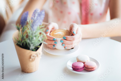 Woman hands holding cup of coffee. Macarons on table and lavender.