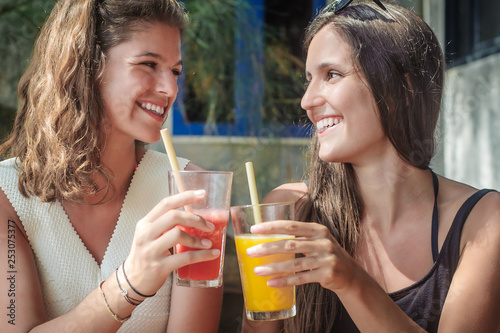 Two girlfriends drinking fruit cocktail on a tropical beach