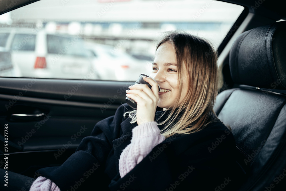 cute girl drinks coffee from a plastic cup in a car with leather seats.