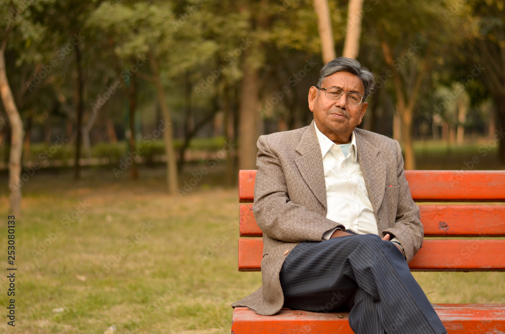 senior-indian-man-sitting-on-a-red-park-bench-wearing-a-tweed-coat-in