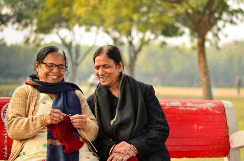 2 senior indian women discussing a sweater knitting and laughing