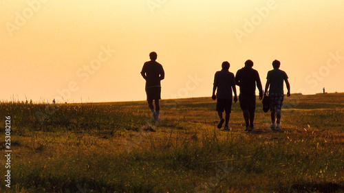 Silhoutte of a team of people friends walking or jogging into the sunset or sunrise near the horizon on a grassland