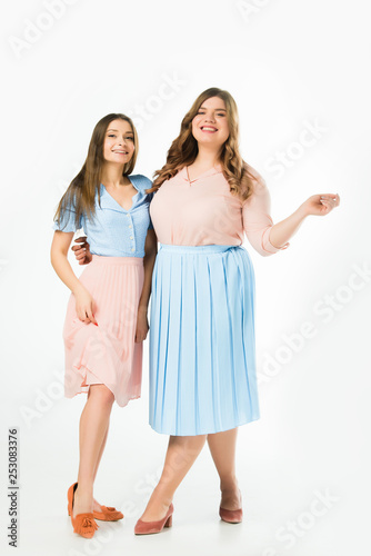 smiling elegant overweight and slim women embracing on white background