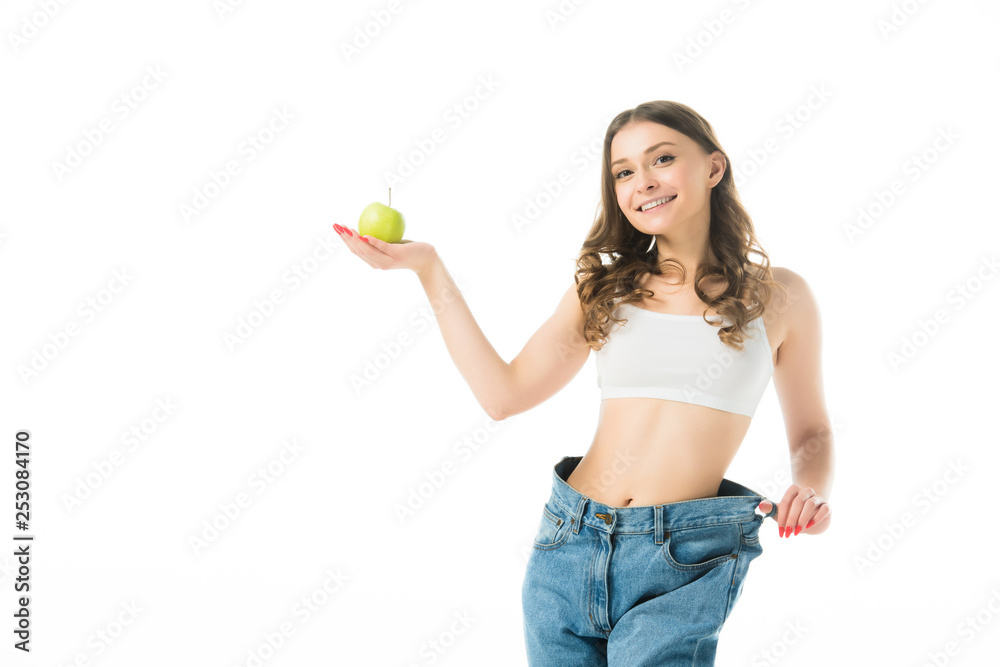 smiling slim young woman in big jeans holding green apple isolated on white smiling slim young woman in big jeans holding green apple isolated on white