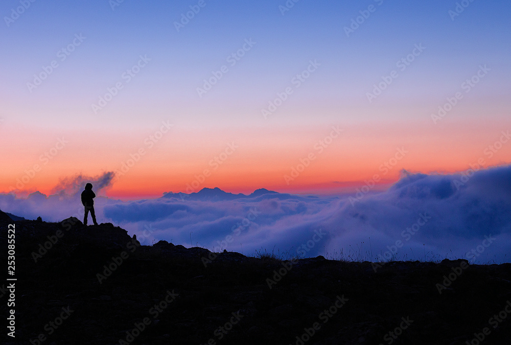 Silhouette of a man standing against the clouds at sunset