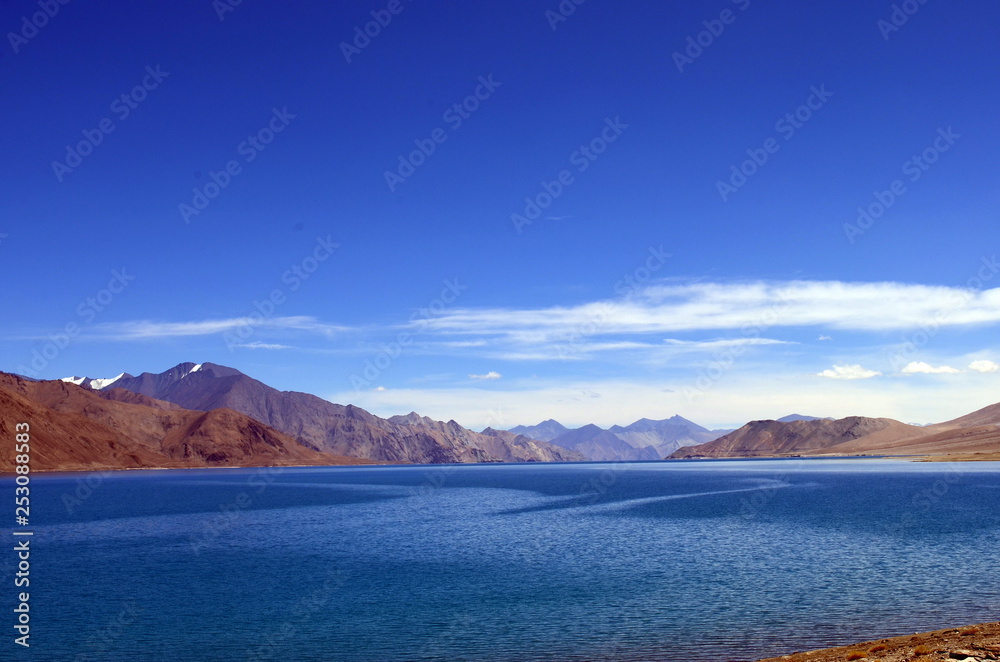 View of Pangong Lake (Tso) from the beachside. The clear blue water stands out amidst skies and Himalayan range. On the border of India and China, this is one of the most recognized lake worldwide