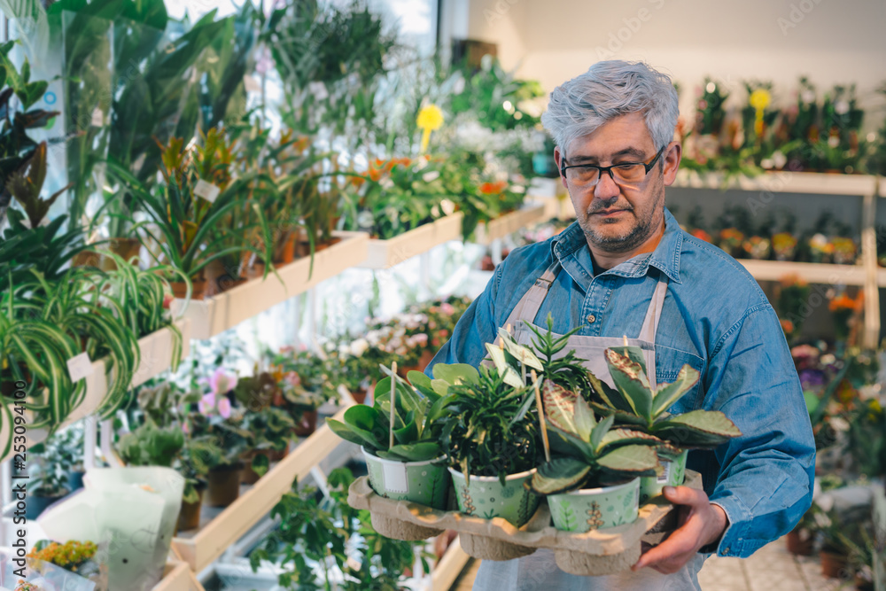 middle aged man holding crate of green plants in flower shop