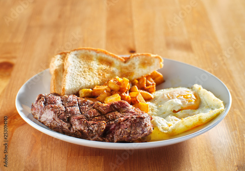steak and eggs breakfast with toast and homestyle potatoes on wooden table