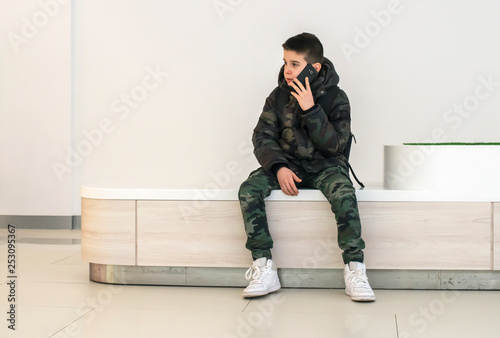 Teenager talking on smartphone in modern commercial center. Technology and communication concept with child in contemporary building interior. © Deyan Georgiev