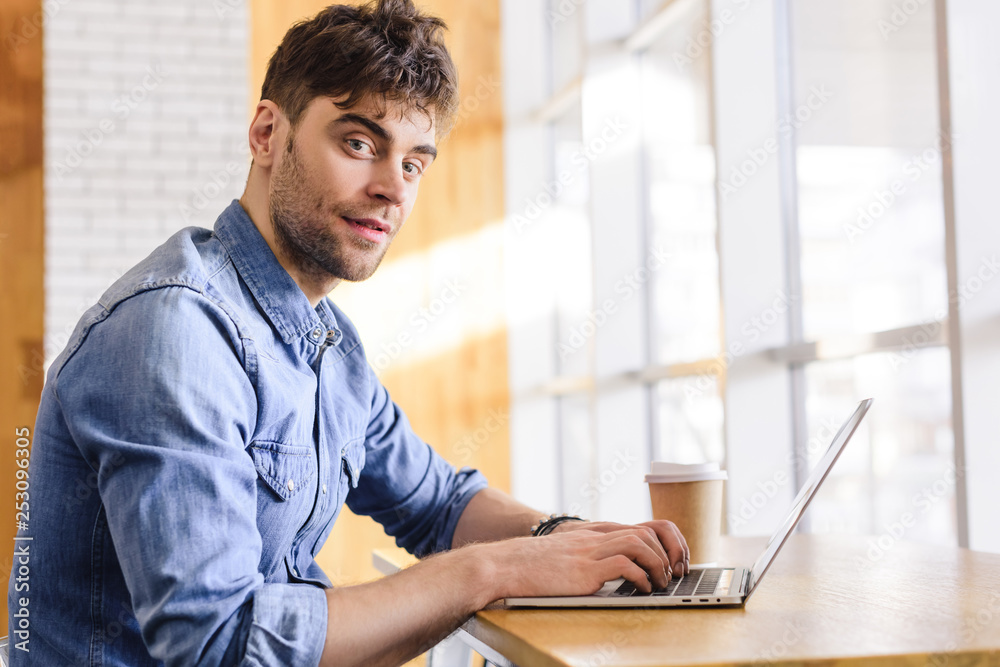 Fototapeta premium handsome man using laptop and looking at camera at cafe