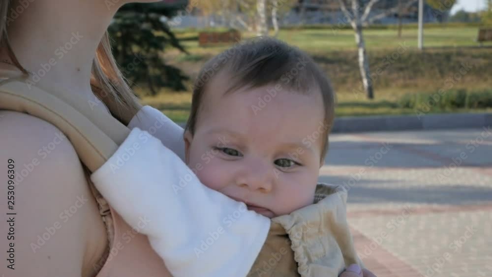 Young happy mom with baby girl in ergo backpack walking in the Park Young happy mom with baby girl in ergo backpack walking in the Park