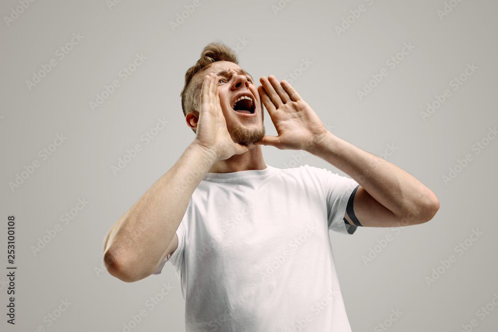 Do not miss. Young casual man shouting. Shout. Crying emotional man screaming on gray studio background. Male half-length portrait. Human emotions, facial expression concept Do not miss. Young casual man shouting. Shout. Crying emotional man screaming on gray studio background. Male half-length portrait. Human emotions, facial expression concept