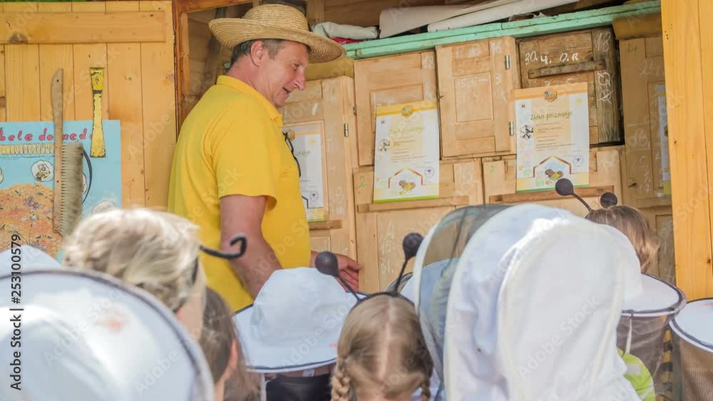 The beekeeper is explaining the children about bees and an apiary. It's a nice summer day and the children are having a field trip.