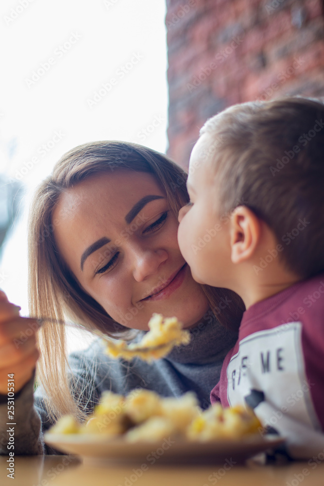 happy family, blonde mother and her beautiful and charismatic little son, the boy is having fun day in a cozy cafe. selective focus, noise effect
