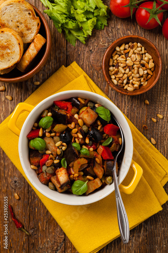 Traditional Italian caponata, served with croutons in a yellow, sunny pot. Decorated with basil and pine nuts.