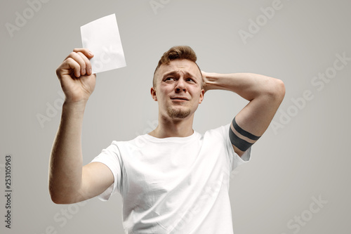 Young caucasian man with a surprised happy expression won a bet on gray studio background. Human facial emotions and betting concept