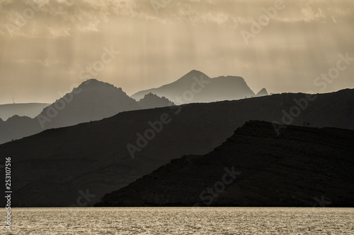 Silhouettes of mountains against the background of the sun. Ru'us al Jibal. Al Hajar Moutains. Musandam. Oman photo