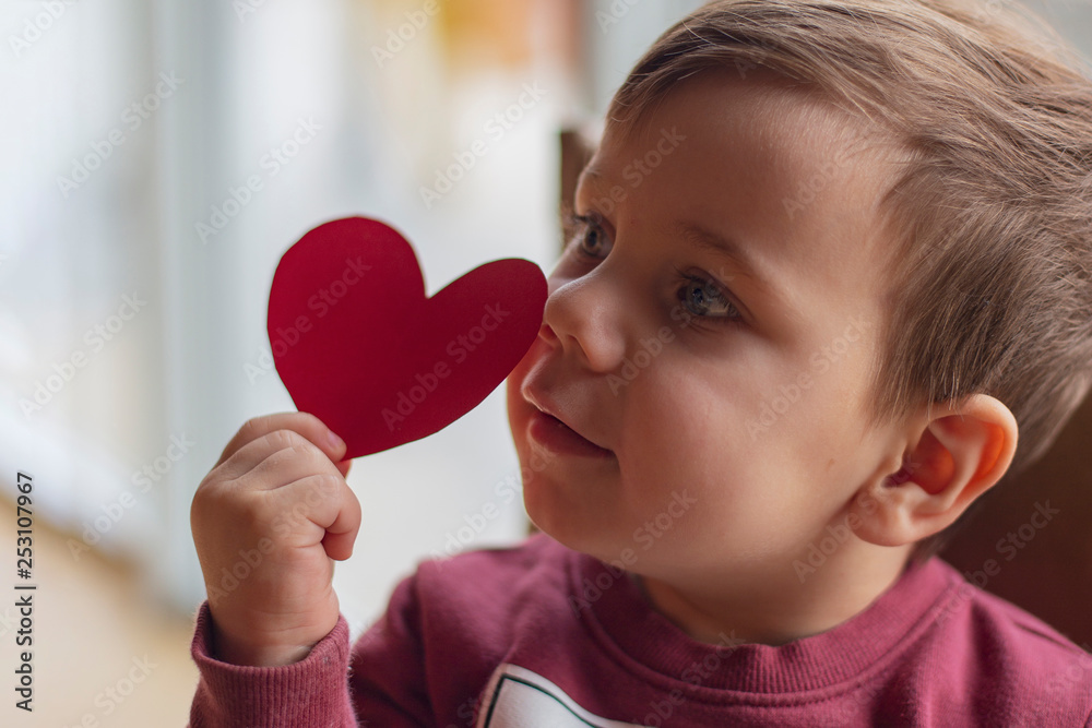 Happy little boy with red paper heart in hand shape loving look to his mother Happy little boy with red paper heart in hand shape loving look to his mother