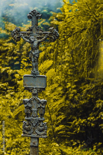 A carved, stone celtic cross in Ireland, with green hills and a blue sky behind. Moss is growing on the stonework which is old.