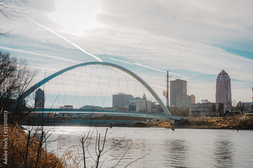 Naklejka premium Downtown Des Moines and the Iowa Women of Achievement Bridge from the banks of the Des Moines River in Des Moines, Iowa