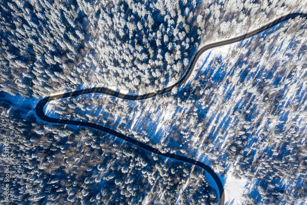 Curvy road in winter forest, view from above