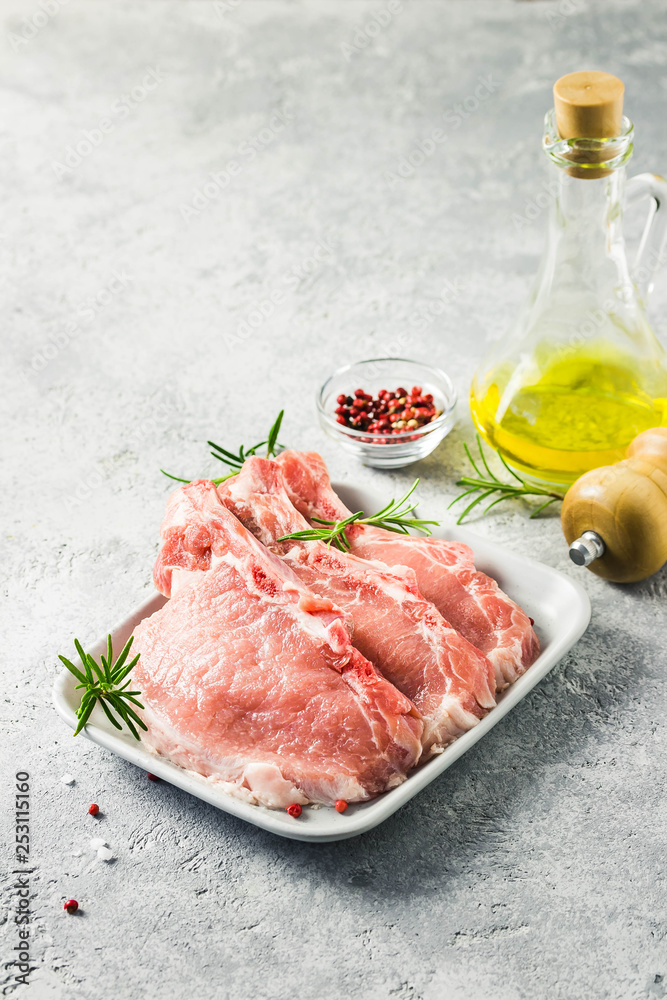 Raw meat, pork cutlets on a plate with rosemary, salt, pepper and olive oil. Selective focus, space for text.