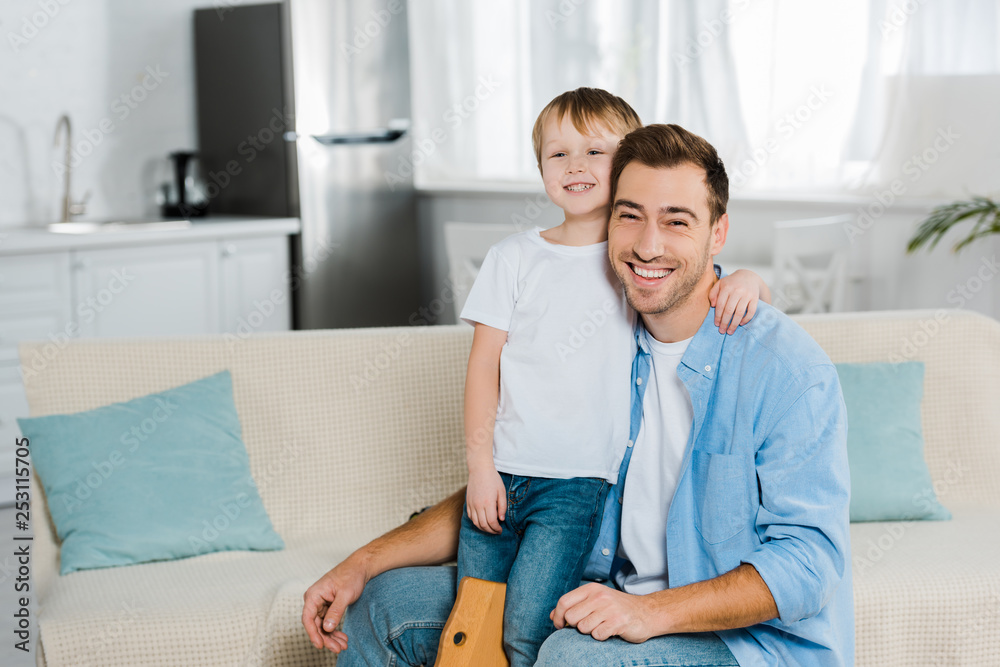 happy father and preschooler son hugging and looking at camera at home happy father and preschooler son hugging and looking at camera at home