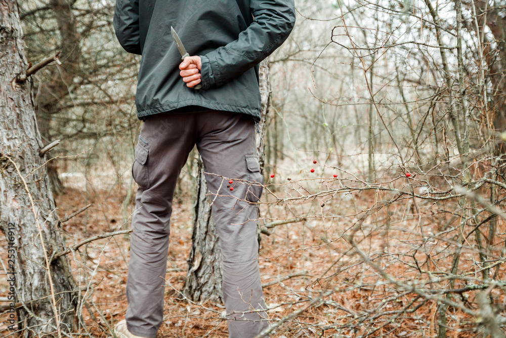 man with knife hiding in the autumn forest and going to make criminal