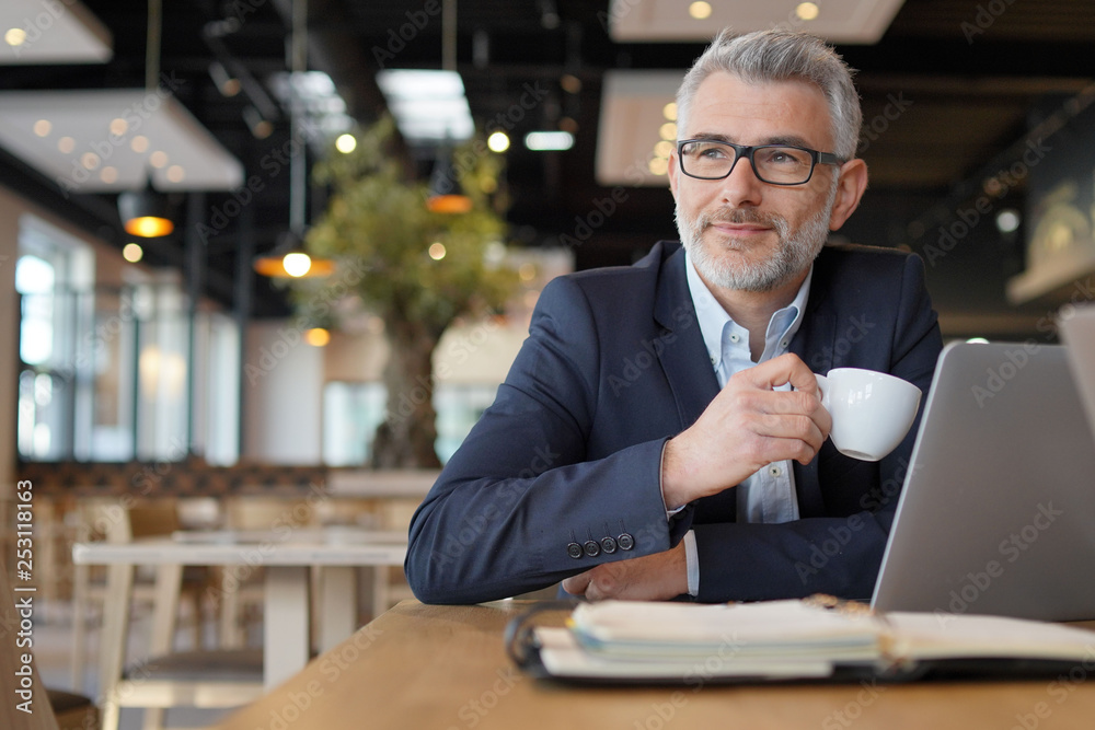 Mature businessman smiling during working coffee break
