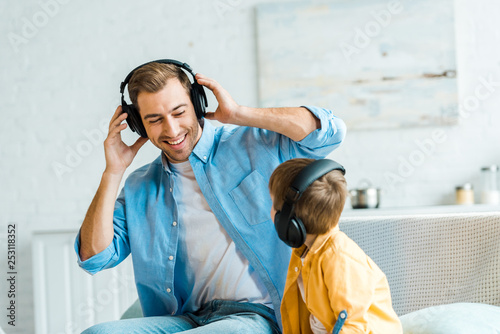 handsome smiling father with preschooler son in headphones listening music at home