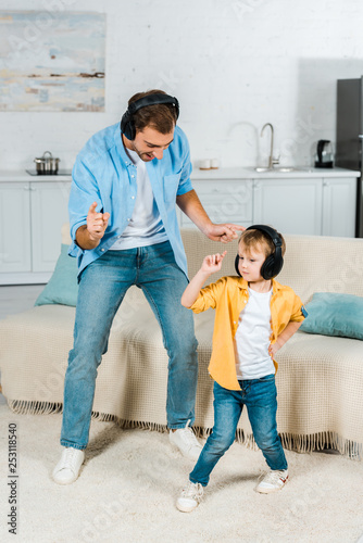 father with preschooler son in headphones listening music and dancing at home