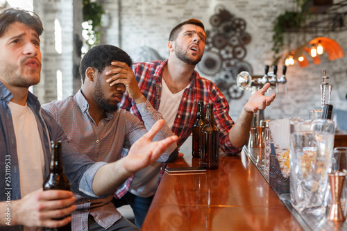 Lost match. Upset friends watching football in sport bar photo