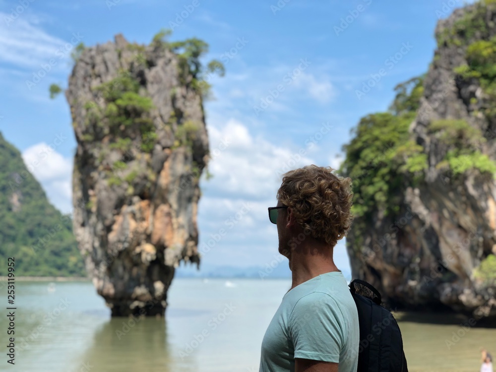 a light-skinned guy in sunglasses and a t-shirt shows his fingers the sign perfectly on the famous James bond island in Thailand, the azure sea and the wonder Islands in the afternoon