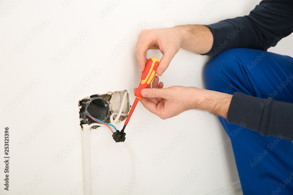 Naklejka premium Electrician with screwdriver repairing power socket indoors, closeup