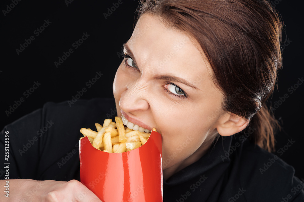 emotional woman eating tasty french fries while looking at camera isolated on black emotional woman eating tasty french fries while looking at camera isolated on black