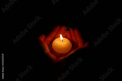 Hands holding a burning candle in dark. Burning candle in the children's hands on a dark background.