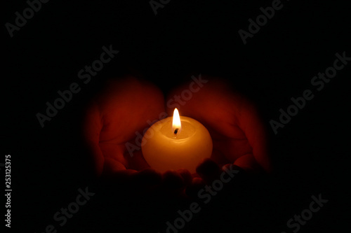 Hands holding a burning candle in dark. Burning candle in the children's hands on a dark background.