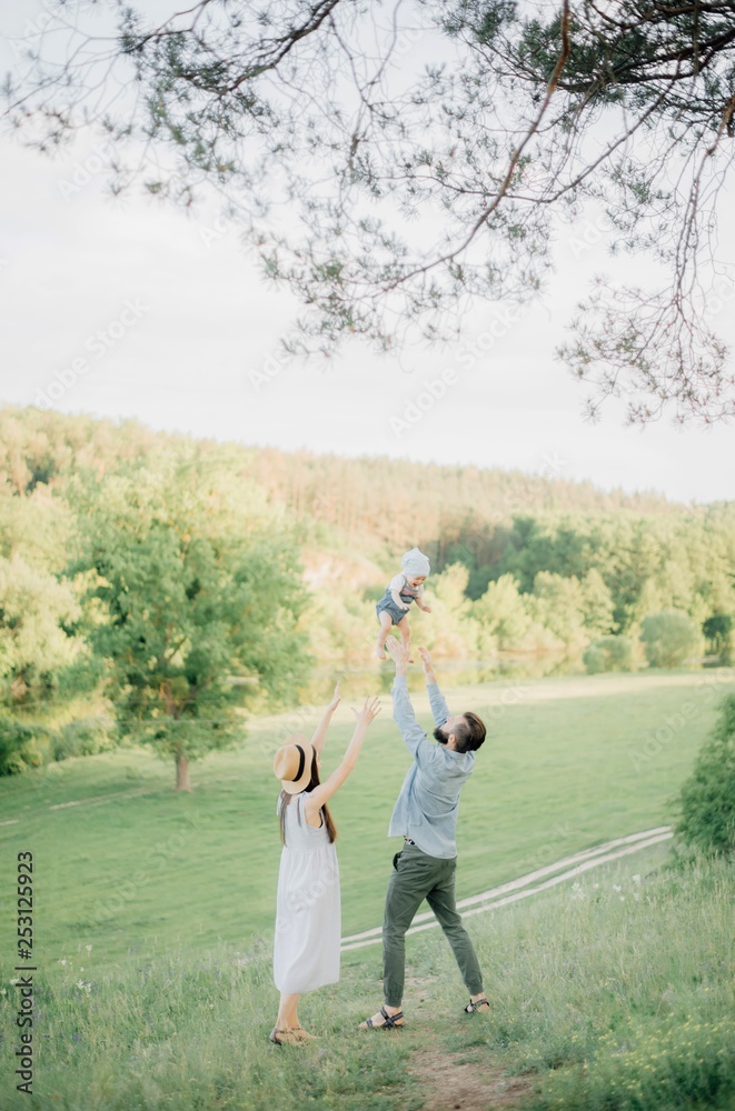 Happy family outdoor in spring. A stylish father with a beard keeps a daughter in his arms with his wife