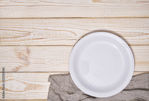 Empty white plate and gray napkin on a wooden background, top view.