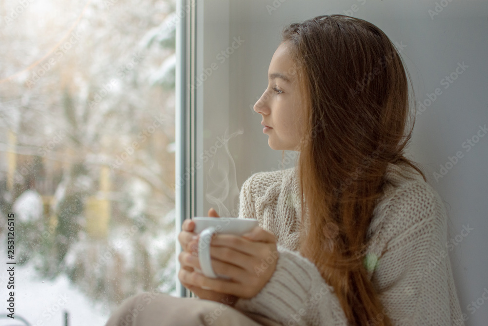 Young woman looking through window enjoys drinking coffee Young woman looking through window enjoys drinking coffee