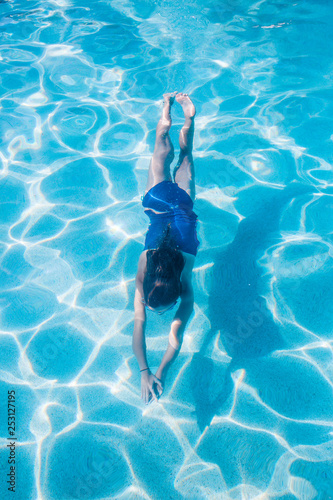 A little girl swimming underwater in an outdoor swimming pool. View from above. Floating through the crystal blue water on a warm summer day © Brocreative