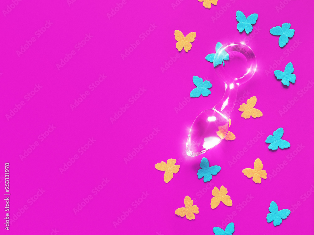 A glass sex toy (butt plug) and blue and yellow felt butterflies are on a fuchsia background.