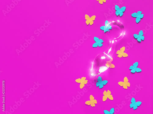 A glass sex toy  butt plug  and blue and yellow felt butterflies are on a fuchsia background.