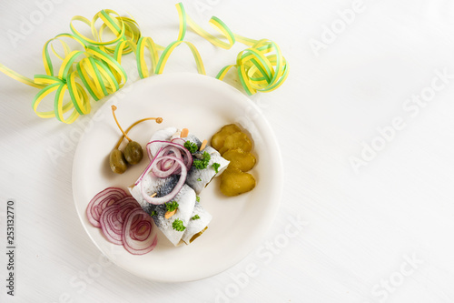 hangover meal, rolled pickled herring, also called rollmops with red onions, gherkins and capers on a white table with paper streamer, high angle view from above, copy space