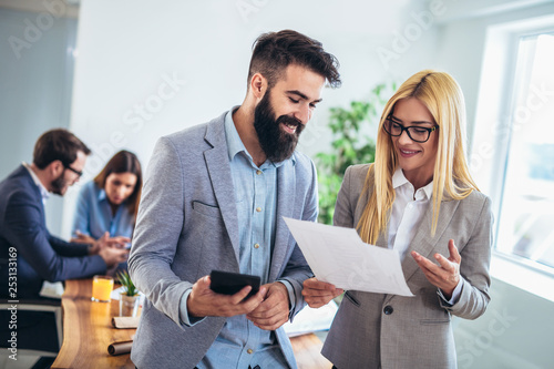 Portrait of two young businesspeople using digital tablet while colleague in background