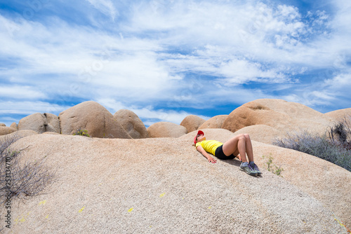 Young woman lying on the hot stone on a sunny day and looking to the sky in Joshua Tree National Park, USA. Freedom and adventure concept.