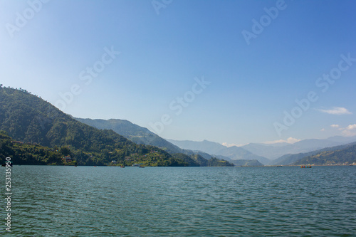 Phewa lake with boats on the background of a green mountain valley under the blue sky, view from the water © Pavel