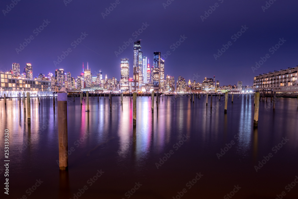 New York City Manhattan Midtown Panorama at Night with Skyscrapers illuminated over Hudson River.