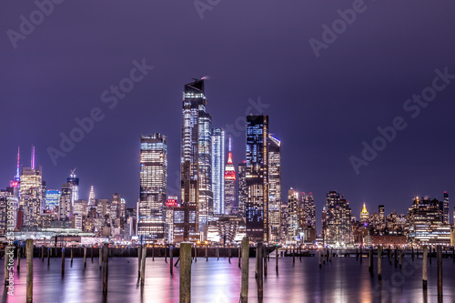 New York City Manhattan Midtown Panorama at Night with Skyscrapers illuminated over Hudson River.